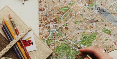 Notebook and glasses next to map with person holding pen in right hand