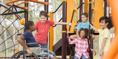 Five children on a colorful playground and smiling and one child is in a wheelchair