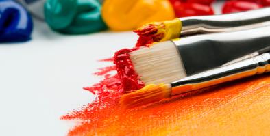 Picture of different colors of paint and paint brushes spilled on a canvas.