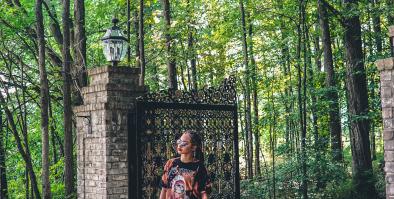 Youth standing in front of an open gate with forest in the background. 