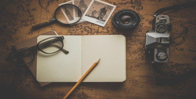 photo of notebook, camera, photos with magnifying glass and glasses scattered on top of a map.