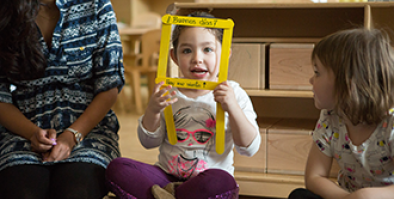 A seated child holding up a frame around their face