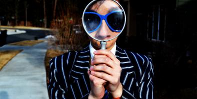 Person with magnifying glass held in front of their face.